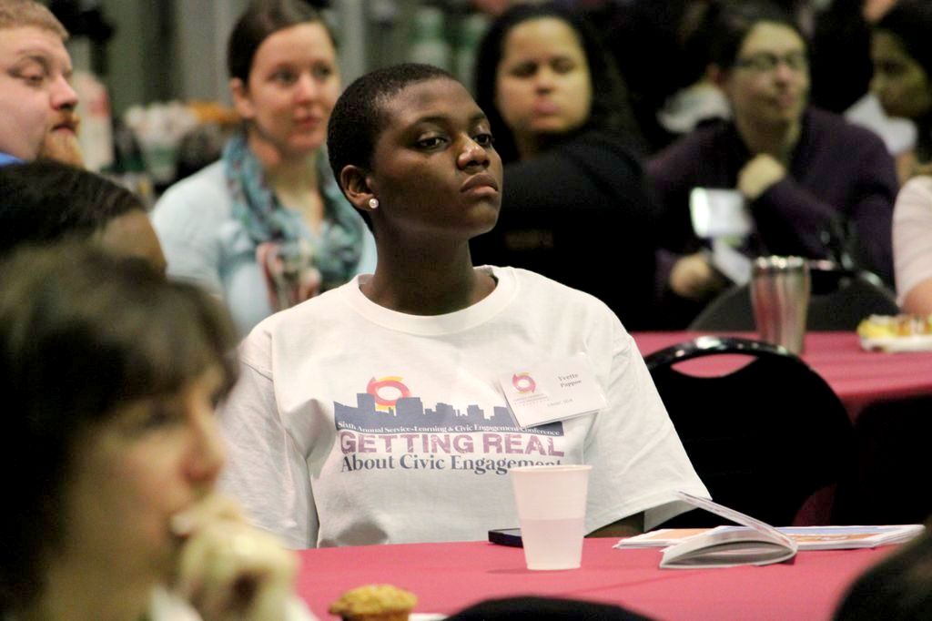 A student wearing a shirt that says "Getting Real About Civic Engagement" watches a presentation.